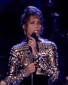 a woman singing into a microphone while wearing a gold and silver jacket