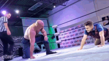 a wrestler is kneeling down in front of another wrestler while a referee looks on