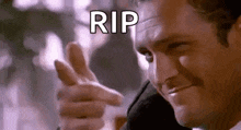 a man in a suit is pointing his finger at the camera and saying `` rip '' .