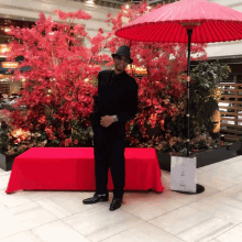 a man in a black suit stands in front of a red table