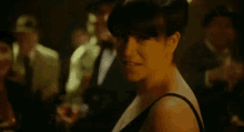 a woman in a black dress and hat is dancing in a dark room with other people .