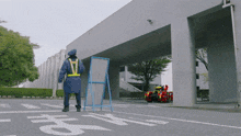 a man wearing a blue jacket and a yellow vest stands next to a sign that says ' a '