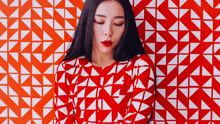 a woman is standing in front of a red and white geometric patterned wall