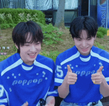 two boys wearing blue shirts with the number 5 giving a thumbs up