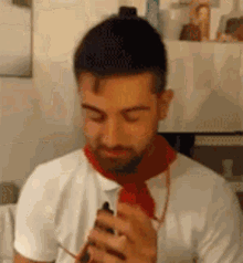 a man with a beard is wearing a red scarf around his neck while holding a cell phone .