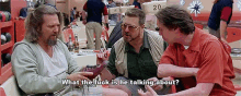 three men are sitting at a table in a bowling alley talking to each other .