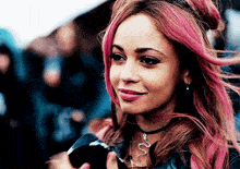 a woman with pink hair and a snake necklace smiles