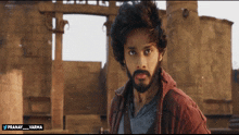 a man with a beard is standing in front of a building with the name pranay varma written below him
