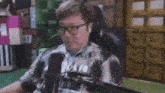 a man wearing glasses and headphones is sitting in front of a microphone in a chair .