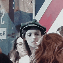 a woman in a green hat is smoking a cigarette in front of a sign that says 2