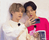 two young men are looking at a cell phone and one of them is wearing a pink shirt that says ' suga ' on it