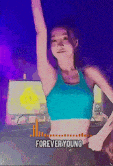 a woman in a blue crop top is dancing in front of a sign that says " forever young "
