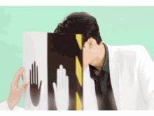 a man in a white jacket covering his face behind a sign