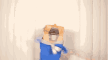 a person is standing in front of a white curtain wearing a blue shirt and a paper bag on their head .