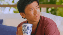 a man is sitting on a couch holding a cup of coffee and making a funny face .