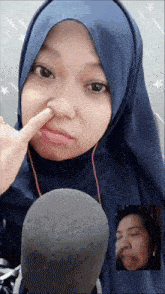 a woman in a blue hijab is making a funny face with her finger