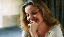 a woman with blonde hair and a ring on her finger smiles