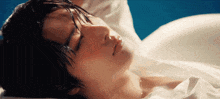 a man is laying on a bed with his eyes closed and a white shirt on