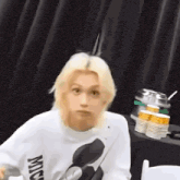 a young man with blonde hair is sitting at a table with a mickey mouse sweatshirt on .
