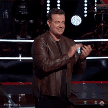 a man wearing a brown leather jacket is applauding on the stage