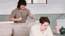 a man is standing next to a boy sitting on a couch and yelling at him .