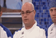 a bald man wearing glasses and a bandana is sitting in front of a group of other men .