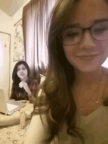 a girl with glasses is smiling while another girl sits behind her