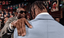a man in a suit and sunglasses is touching another man 's shoulder