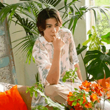 a man in a floral shirt sits on a couch in front of plants