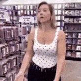 a woman in a white tank top is standing in a store looking at something .