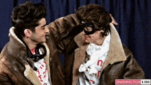 a man wearing a goggles and a jacket talks to another man