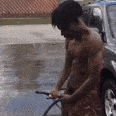 a shirtless man is washing a car with a water hose