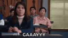 a group of people are sitting at desks in a classroom and a woman is making a funny face .
