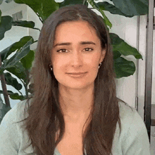 a close up of a woman 's face with long hair and a plant in the background .