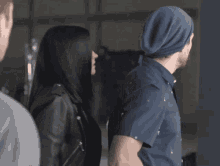 a woman in a leather jacket stands next to a man in a blue hat