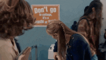 a woman braids her hair in front of a sign that says do n't go to college
