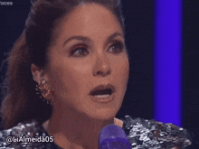 a woman in a sequined top is speaking into a purple microphone