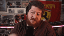 a man with a beard is talking into a microphone in front of a ferrari banner