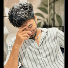 a man wearing a striped shirt is smiling and covering his face