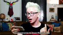 a man with green hair and glasses is looking at his phone and says i need everyone to know that i 'm cute
