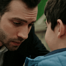 a man and a boy are looking at each other and the boy is wearing a blue jacket