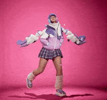 a girl in a plaid skirt and a purple jacket is dancing on a pink background