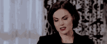 a woman in a black jacket and red lipstick is making a face .