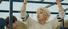 a man with blonde hair is hanging from a metal structure while another man looks on .
