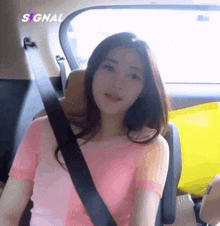 a woman in a pink shirt is sitting in the back seat of a car with a seat belt on .