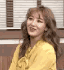 a woman in a yellow shirt is sitting on a bench in front of a window and smiling .