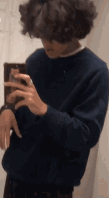 a young man with curly hair is taking a picture of himself in a mirror .
