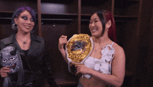 two women are standing in a locker room and one is holding a gold belt that says ' wwe ' on it