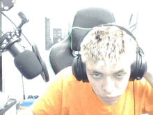 a young man wearing headphones and an orange shirt looks at the camera