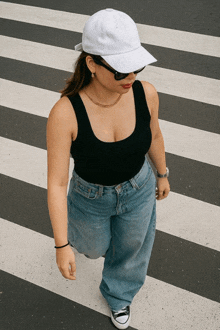 a woman wearing a black tank top and blue jeans is crossing a zebra crossing